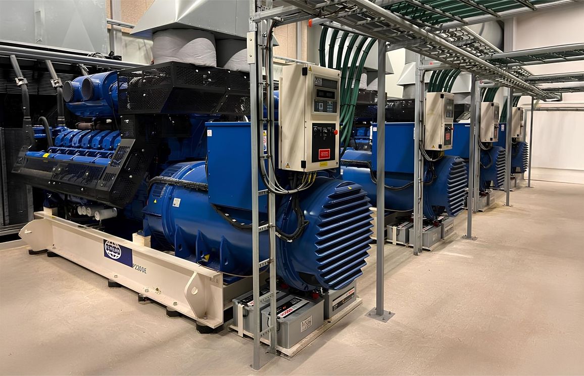 Mehrere große blaue Industriemaschinen mit weißen Basen in einer Halle, umgeben von Metallrohren und Steuerkästen.